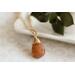 Sunstone necklace, orange briolette in 14K gold, on white dish with green leaves.