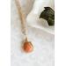 Sunstone necklace, orange briolette in 14K gold, on white dish with green leaves.