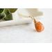 Sunstone necklace, orange briolette in 14K gold, on white dish with green leaves.