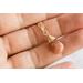 Sunstone necklace, orange briolette in 14K gold, held in hand on white background.