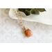 Sunstone necklace, orange briolette in 14K gold, on white dish with green leaves.