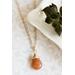 Sunstone necklace, orange briolette in 14K gold, on white dish with green leaves.