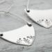 Handcrafted sterling silver fern-stamped hoop earrings on a wooden surface, showcasing elegant leaf designs. 
