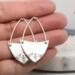 Handcrafted sterling silver fern-stamped hoop earrings held in a hand showcasing elegant leaf designs. 
