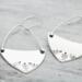 Handcrafted sterling silver fern-stamped hoop earrings on a wooden surface, showcasing elegant leaf designs. 
