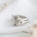  Three sterling silver stackable rings with lowercase initials "a," heart, and "t" on a white  background with dried flowers

