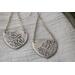 Sterling silver trillion shape imprinted with a mandala design hanging from sterling silver chain from two corners and a sterling ear wire. 