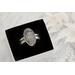 Close-up of a sterling silver wildflower ring with intricate floral etching, displayed in a black velvet box.

