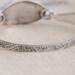 Handcrafted sterling silver wildflower oval cuff bracelet from Alaska, with textured band, on floral paper. 
