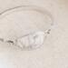 Handcrafted sterling silver wildflower oval cuff bracelet from Alaska, with textured band, on floral paper. 
