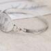 Handcrafted sterling silver wildflower oval cuff bracelet from Alaska, with textured band, on floral paper. 
