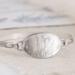 Handcrafted sterling silver wildflower oval cuff bracelet from Alaska, with textured band, on floral paper. 
