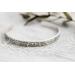 A single sterling silver cuff bracelet with intricate floral engravings, styled with soft natural elements in the background.