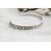 A single sterling silver cuff bracelet with intricate floral engravings, styled with soft natural elements in the background.