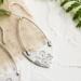Handcrafted sterling silver Art Nouveau floral hoop earrings on a textured background with greenery.
