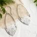 Handcrafted sterling silver Art Nouveau floral hoop earrings on a textured background with greenery.
