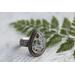 Pear shaped clear agate stone with flecks of greens blues copper in a sterling silver bezel surrounded by beaded wire on floral comfort band