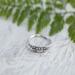 Close-up of vintage sterling silver leaf ring on white wood, eco-friendly, sizes 3-10.  
