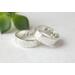 "Two silver bands with personalized engraving, 'JOHN' and 'PSALMS" visible, on a white fabric with green leaves in the background."
