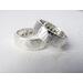 "Two silver bands with personalized engraving, 'JOHN' and 'PSALMS" visible, on a white fabric background."
