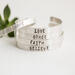 Five sterling silver bracelets with words HOPE, LOVE, GRACE, FAITH, BELIEVE, on a white surface with a green succulent in the background.
