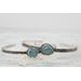 Silver bracelet with floral engravings, featuring a oval blue aquamarine on a light wood surface with scattered white baby's breath flower.
