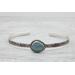 Silver bracelet with floral engravings, featuring a oval blue aquamarine on a light wood surface with scattered white baby's breath flower.
