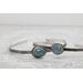 Silver bracelet with floral engravings, featuring a oval blue aquamarine on a light wood surface with scattered white baby's breath flower.
