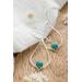 "Pair of silver drop earrings with turquoise gemstones, resting on a white fabric with dried flowers on a wooden surface."