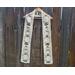 White scarf with snowmen along the length. It is on a hanger in front of a wooden fence.