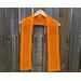 Orange Diagonal Crochet Scarf display on a hanger in front of a wooden fence.