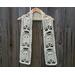 White scarf with ghosts along the length. It is on a hanger in front of a wooden fence.