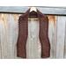 Display of the Zig Zag Crochet Scarf on a hanger in front of a wooden fence.