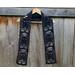 Black scarf with ghosts along the length. It is on a hanger in front of a wooden fence.