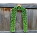 Variegated green scarf with trees along the length. It is on a hanger in front of a wooden fence.