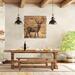 This is a large rustic deer wood wall hanging over a large dinning room table. The table shows wine bottles and party food. 