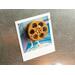 front view of a gold miniature movie reel magnet holding up a polaroid picture on fridge