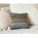 This 100% wool, hand-knit decorative throw pillow with pastel stripes pops against an off-white, shabby chic, boho-style couch.