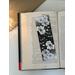 black and white floral bookmark on a book on a white table. Light brown table runner with fairy lights in a jar