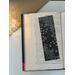 black and white flower bookmark on a book on a white table. Light brown table runner with fairy lights in a jar