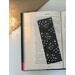 laminated bookmark on a book on a white table. Light brown table runner with fairy lights in a jar