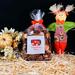 A bag of Pumpkin Spice Potpourri by Irish Twins Potpourri Co on a black background surrounded by hay, a fall bouquet and a scarecrow nearby.