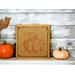 A rustic burlap wood sign with a oranged stenciled pumpkin on it.