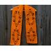 Orange scarf with leaves along the length. It is on a hanger in front of a wooden fence.
