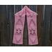 Pink scarf with hearts along the length. It is on a hanger in front of a wooden fence.