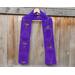 Purple scarf with hearts along the length. It is on a hanger in front of a wooden fence.