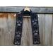 Black scarf with ghosts along the length. It is on a hanger in front of a wooden fence.
