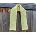 Display of the V-stitch Crochet Scarf on a hanger in front of a wooden fence.