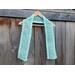 Display of the Diagonal Crochet Scarf on a hanger in front of a wooden fence.