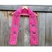 Display of the Mom Crochet Scarf on a hanger in front of a wooden fence.